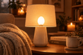 White eggshell light bulb glowing in a cozy living room corner with blankets and a steaming mug